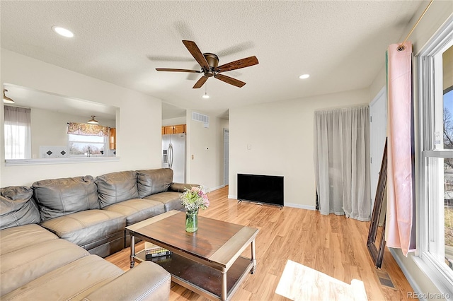 living room featuring visible vents, a textured ceiling, a ceiling fan, and light wood finished floors