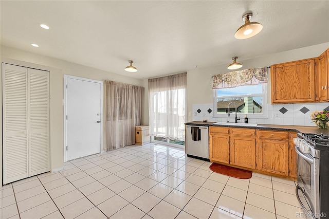 kitchen with a sink, appliances with stainless steel finishes, brown cabinetry, and light tile patterned floors