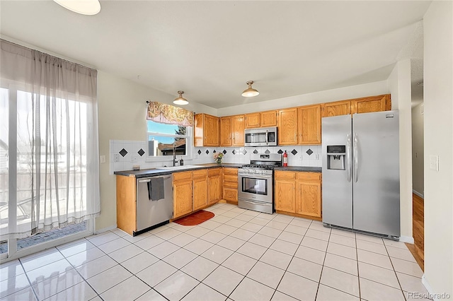 kitchen with light tile patterned floors, stainless steel appliances, dark countertops, and decorative backsplash