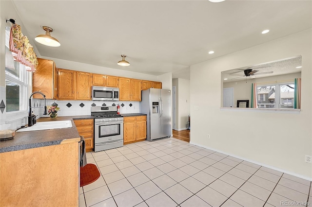 kitchen with dark countertops, ceiling fan, decorative backsplash, appliances with stainless steel finishes, and a sink