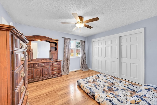 bedroom with ceiling fan, baseboards, light wood-style floors, a closet, and a textured ceiling