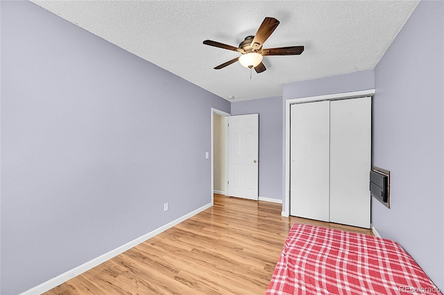 unfurnished bedroom with a textured ceiling, a closet, light wood finished floors, baseboards, and ceiling fan