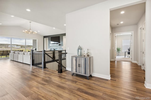 hallway featuring baseboards, lofted ceiling, wood finished floors, and a notable chandelier