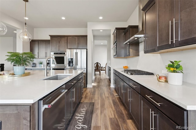 kitchen with dark brown cabinetry, appliances with stainless steel finishes, a sink, light countertops, and dark wood finished floors
