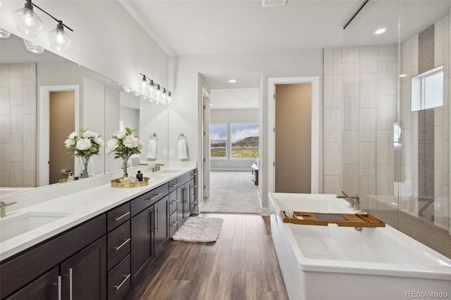 full bathroom with double vanity, a sink, a freestanding bath, and wood finished floors