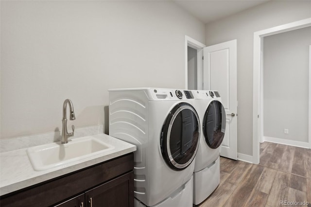 washroom with cabinet space, a sink, separate washer and dryer, baseboards, and light wood-type flooring