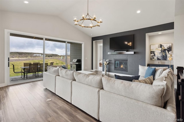 living room with a notable chandelier, a glass covered fireplace, recessed lighting, wood finished floors, and vaulted ceiling