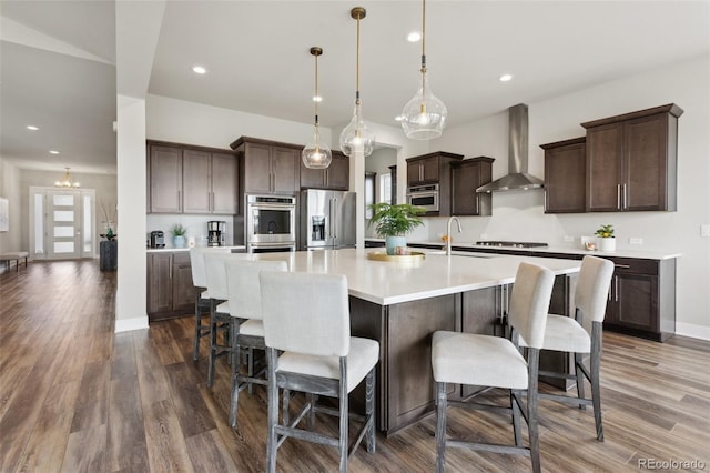 kitchen with a sink, dark brown cabinetry, wall chimney range hood, stovetop, and high end refrigerator