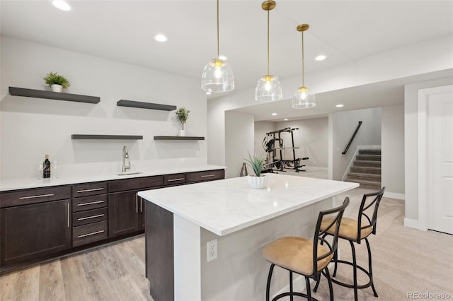 kitchen featuring a breakfast bar area, open shelves, dark brown cabinets, a sink, and recessed lighting