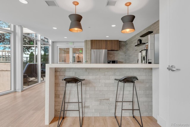 kitchen with a kitchen breakfast bar, decorative light fixtures, stainless steel refrigerator, and kitchen peninsula