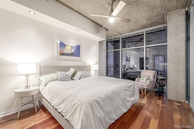 bedroom with wood-type flooring, ceiling fan, and a wall of windows