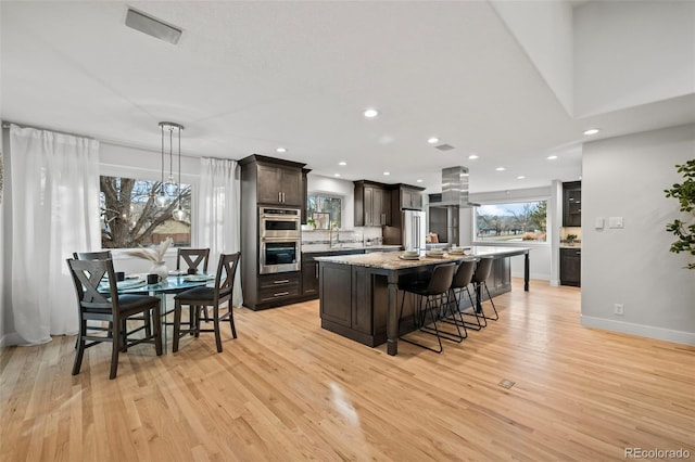 kitchen featuring dark brown cabinets, double oven, decorative light fixtures, a center island, and light hardwood / wood-style floors