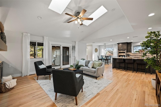 living room featuring light hardwood / wood-style flooring, ceiling fan, and vaulted ceiling with skylight