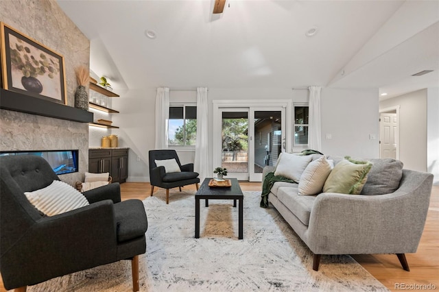 living room with ceiling fan, a large fireplace, lofted ceiling, and light wood-type flooring