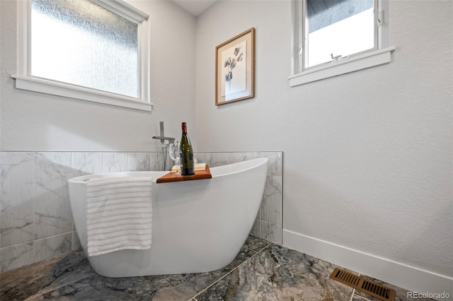 bathroom with a bathing tub, tile walls, and a healthy amount of sunlight