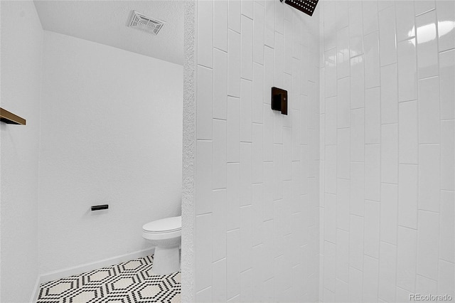 bathroom with a textured ceiling, toilet, and tiled shower