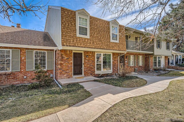 view of front of property with a balcony, brick siding, and a shingled roof