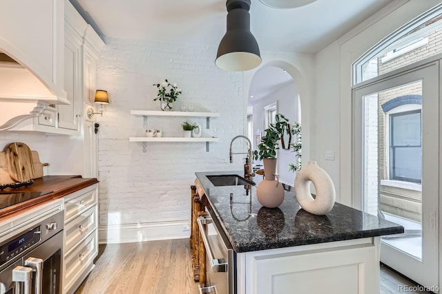 kitchen featuring sink, white cabinetry, an island with sink, dark stone counters, and oven