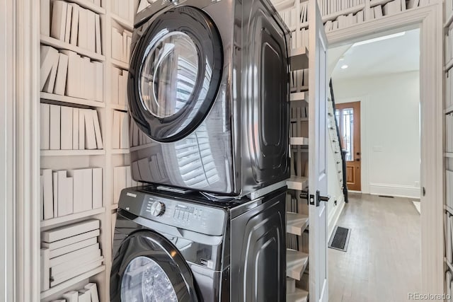 clothes washing area featuring cabinets, stacked washer / dryer, and wood-type flooring