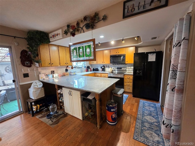 604 S Xenon Ct, Lakewood, CO 80228 - kitchen featuring black appliances, a peninsula, light wood-style flooring, a textured ceiling, and decorative backsplash