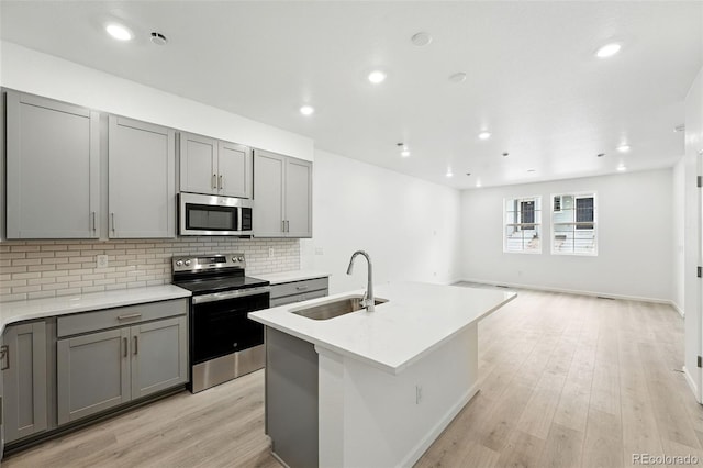 17115 W 91st Ln, Arvada, CO 80007 - kitchen featuring appliances with stainless steel finishes, a sink, gray cabinetry, tasteful backsplash, and light wood-type flooring