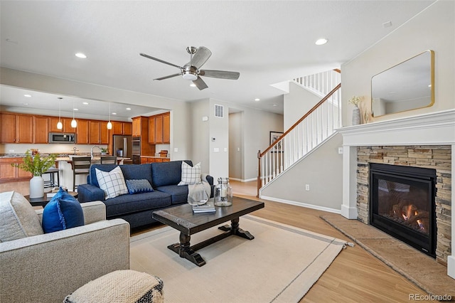 12623 Canoe St, Firestone, CO 80504 - living room featuring light wood-style flooring, ceiling fan, stairway, a stone fireplace, and recessed lighting