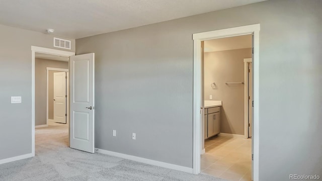 unfurnished bedroom with a walk in closet, ensuite bathroom, and light colored carpet