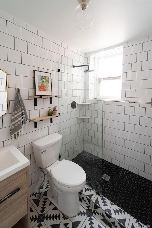 full bath featuring toilet, vanity, tiled shower, and tile walls