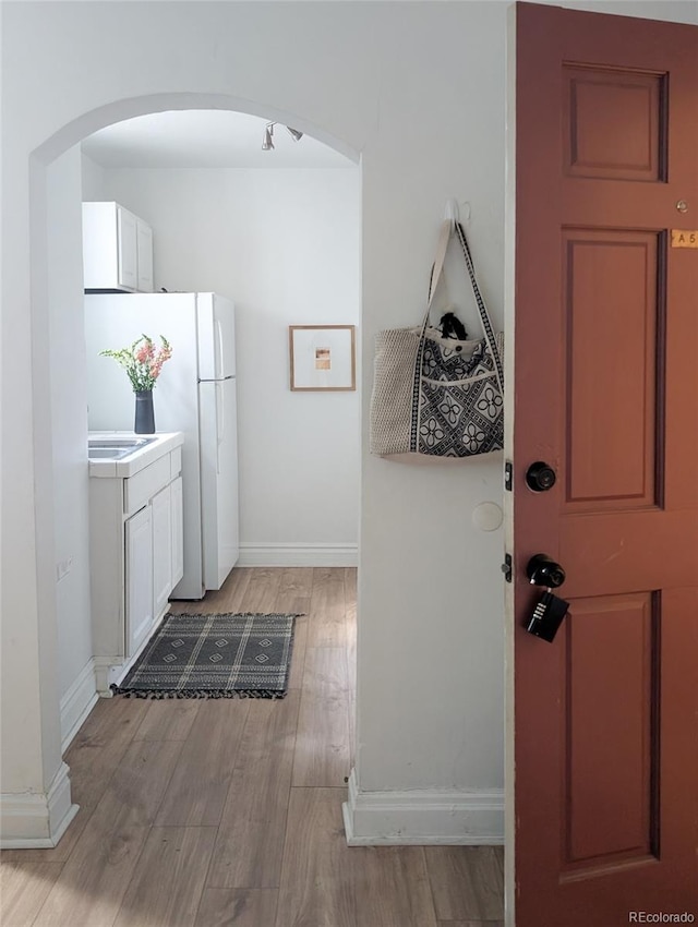kitchen featuring light countertops, light wood finished floors, white cabinetry, baseboards, and arched walkways