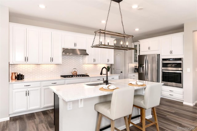 kitchen featuring a center island with sink, stainless steel appliances, hanging light fixtures, white cabinets, and sink