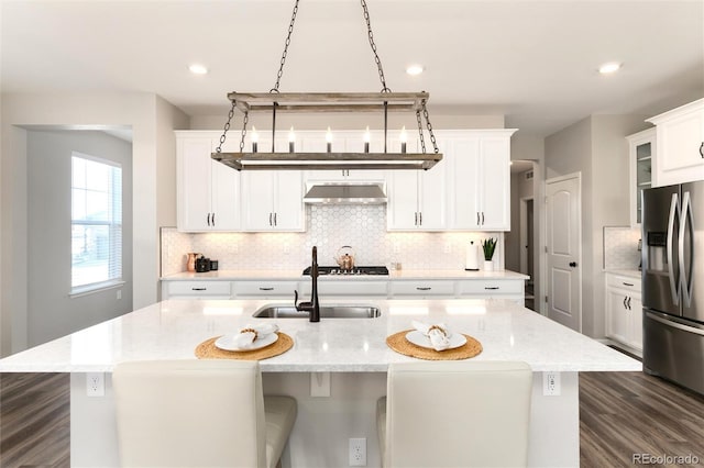 kitchen featuring light stone countertops, stainless steel fridge, a center island with sink, and ventilation hood