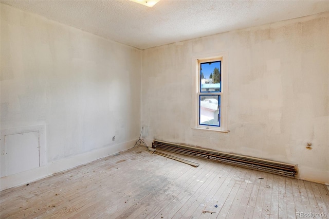 empty room featuring hardwood / wood-style floors, a textured ceiling, and a baseboard heating unit