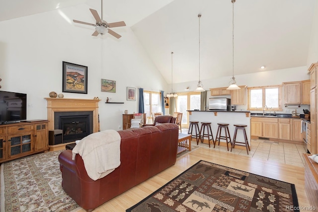 living room featuring ceiling fan with notable chandelier, sink, high vaulted ceiling, and light hardwood / wood-style flooring