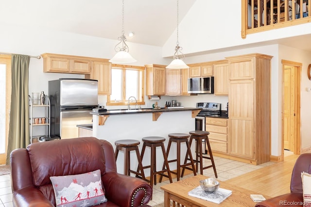 kitchen with stainless steel appliances, decorative light fixtures, a breakfast bar area, light brown cabinetry, and light tile patterned flooring