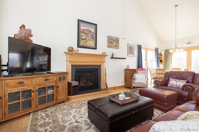 living room with a chandelier, high vaulted ceiling, a glass covered fireplace, and light wood-style floors