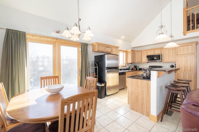 kitchen with light tile patterned floors, dark countertops, appliances with stainless steel finishes, hanging light fixtures, and light brown cabinetry