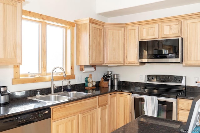 kitchen with light brown cabinets, appliances with stainless steel finishes, dark stone counters, and a sink