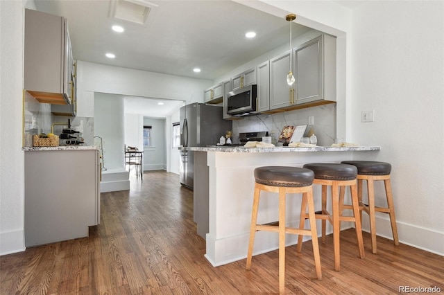 kitchen with gray cabinetry, stainless steel appliances, a breakfast bar, dark wood-type flooring, and backsplash