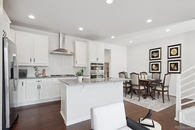 kitchen featuring stainless steel appliances, light stone countertops, dark wood finished floors, and wall chimney range hood