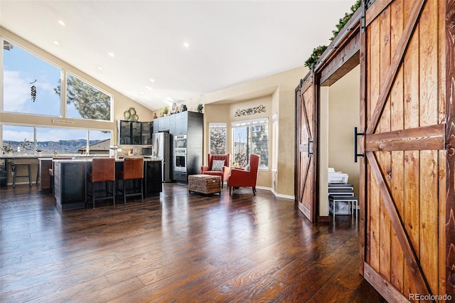 interior space featuring high vaulted ceiling, dark wood-style flooring, baseboards, and a barn door