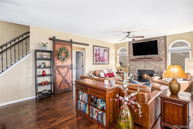 living area with a barn door, dark wood finished floors, ceiling fan, stairway, and a fireplace