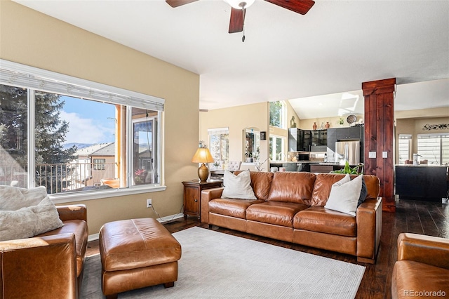 living area featuring lofted ceiling, a ceiling fan, baseboards, dark wood-style floors, and decorative columns