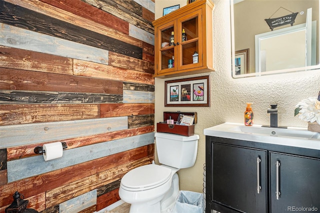 half bathroom featuring wood walls, vanity, and toilet