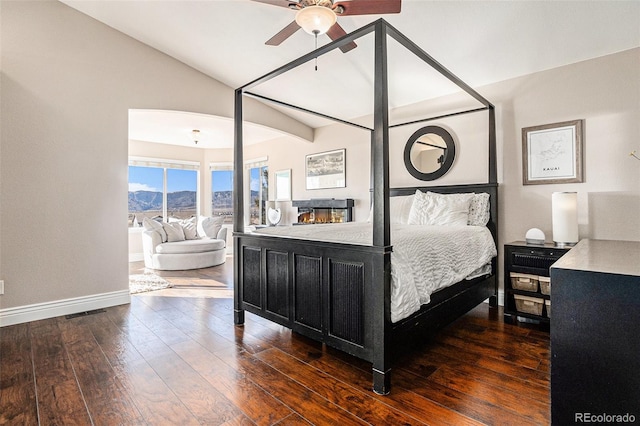 bedroom with a mountain view, baseboards, vaulted ceiling, a lit fireplace, and wood-type flooring