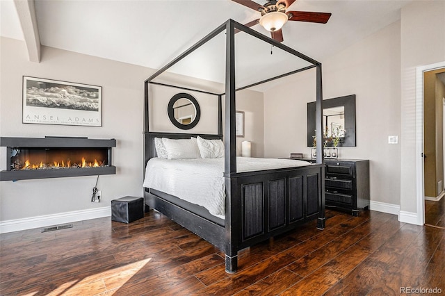 bedroom featuring lofted ceiling, visible vents, wood finished floors, a lit fireplace, and baseboards