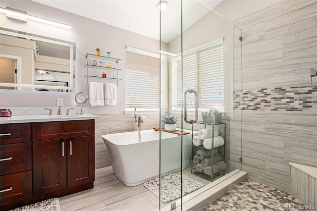 bathroom with a stall shower, a soaking tub, vanity, and tile walls