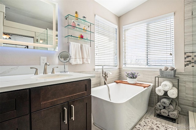 full bath featuring lofted ceiling, a soaking tub, vanity, and tile walls