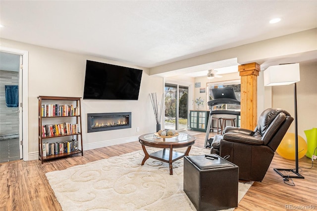 living area featuring baseboards, wood finished floors, a glass covered fireplace, and ornate columns