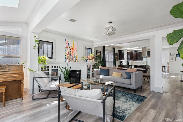 561 Cook St, Denver, CO 80206 - living room featuring light wood-style floors, a chandelier, a glass covered fireplace, baseboards, and crown molding