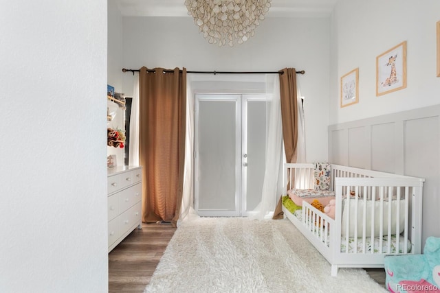 561 Cook St, Denver, CO 80206 - bedroom featuring wood finished floors, a crib, a decorative wall, a wainscoted wall, and a chandelier